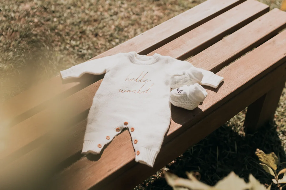 Gestrickter Babyanzug mit Schühchen auf einer Holzbank