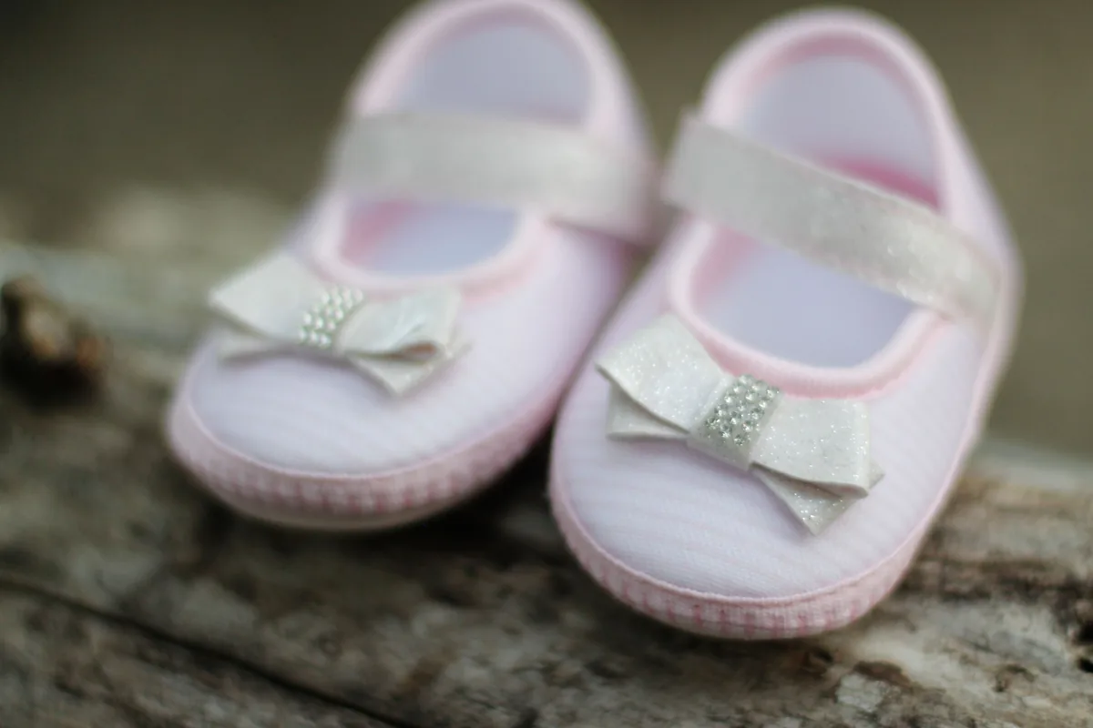 Ein Paar zarte rosa Babyschuhe mit Schleife auf Holz
