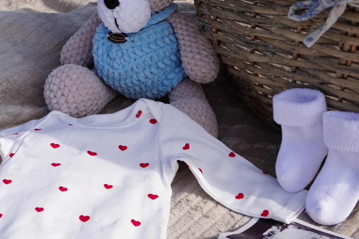 Ein weißer Babybody, ein Teddy und Ultraschallbilder liegen auf einer Decke