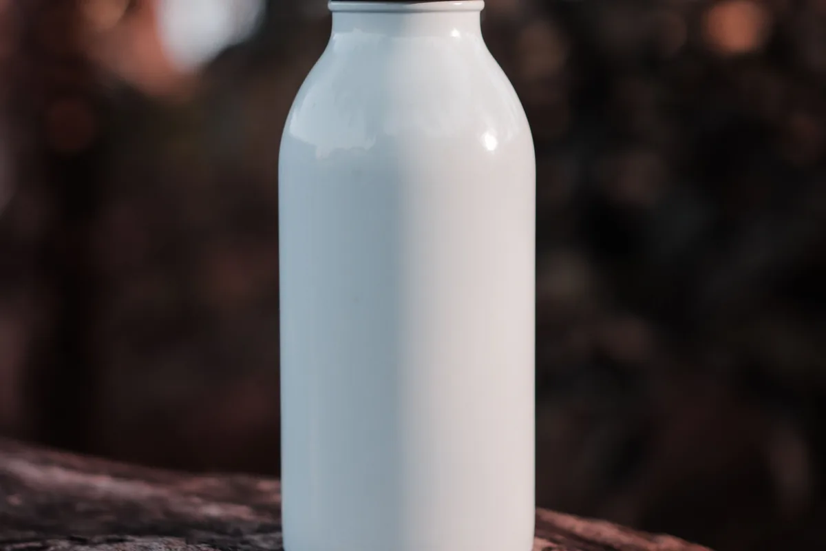 Eine weiße Flasche mit Metallverschluss steht auf einem Holzstamm