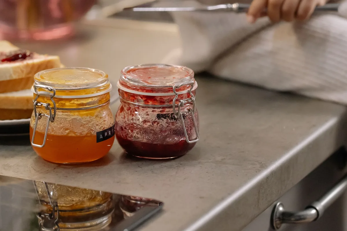 Zwei Gläser mit Marmelade auf einer Küchenzeile, im Hintergrund greift eine Kinderhand nach einem Messer