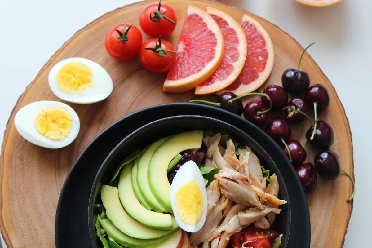 Ein Holzbrett mit gekochten Eiern, Tomaten, Grapefruit, Kirschen und einer Schale mit Salat