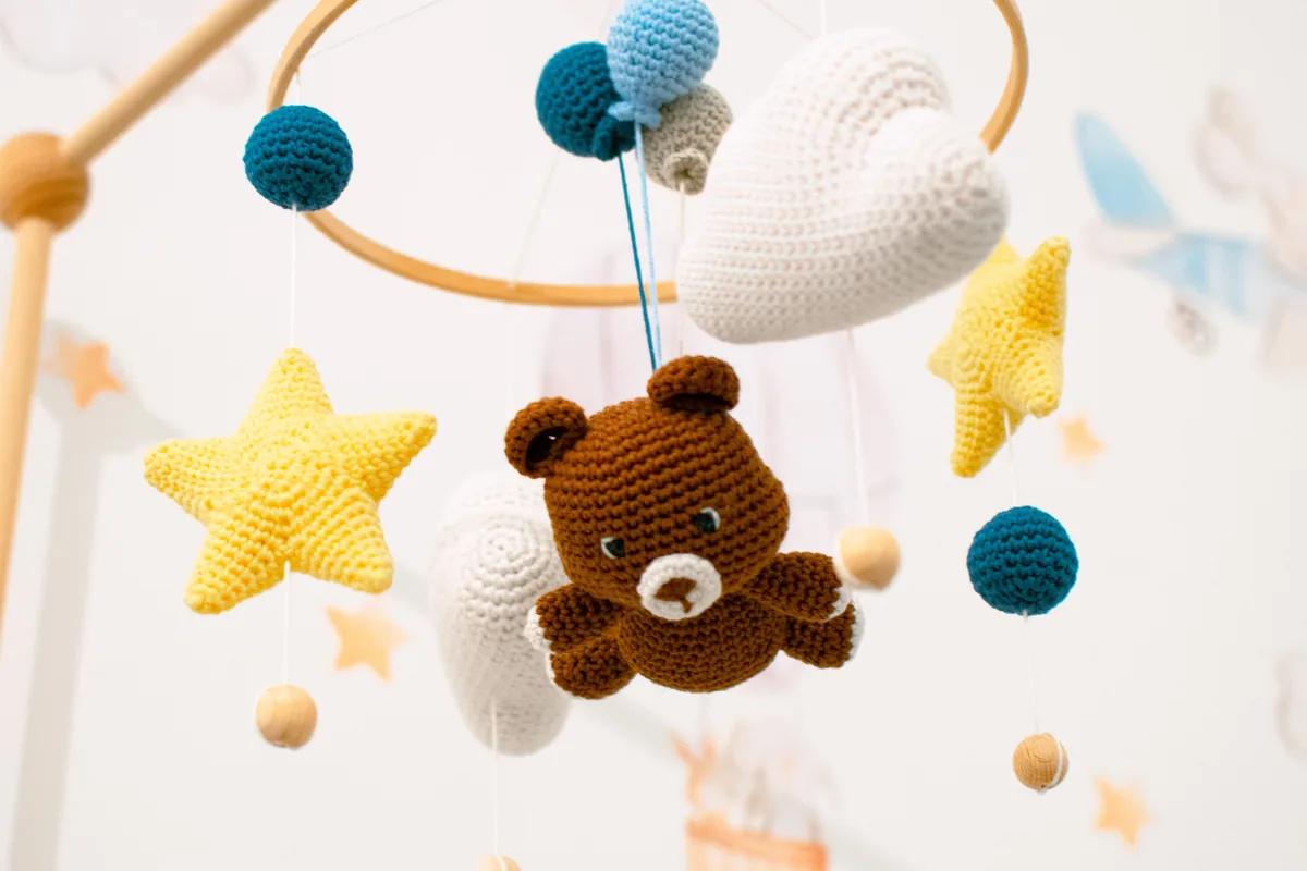 Ein gehäkeltes Mobile mit Bär, Sternen und Wolken hängt über einem Kinderbett