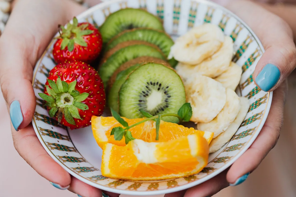 Zwei Hände halten eine Schale mit Erdbeeren, Kiwi, Banane und Orange