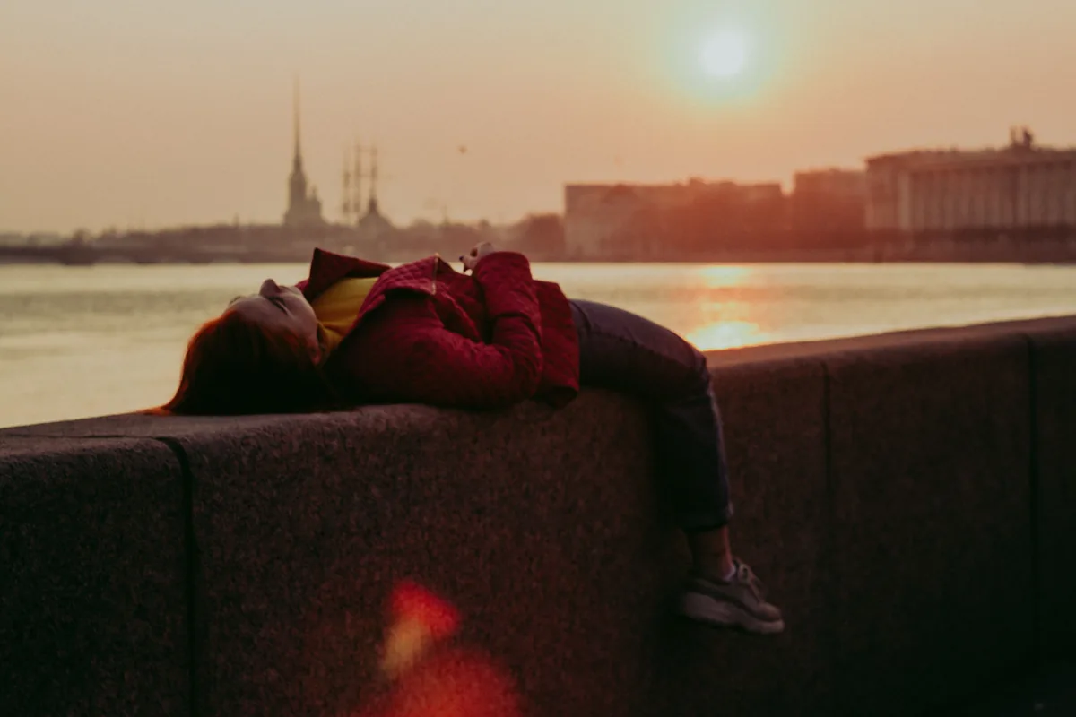 Eine Person liegt ausgestreckt auf einer Mauer, im Hintergrund geht die Sonne unter